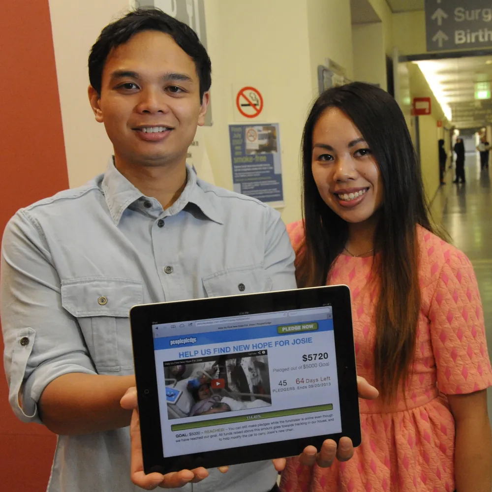 Matthew Alberto and Phuong Nguyen in a hospital corridor in 2013, holding a tablet that shows a PeoplePledge fundraiser